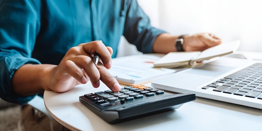 Person berechnet Finanzen mit Taschenrechner und Laptop am Schreibtisch