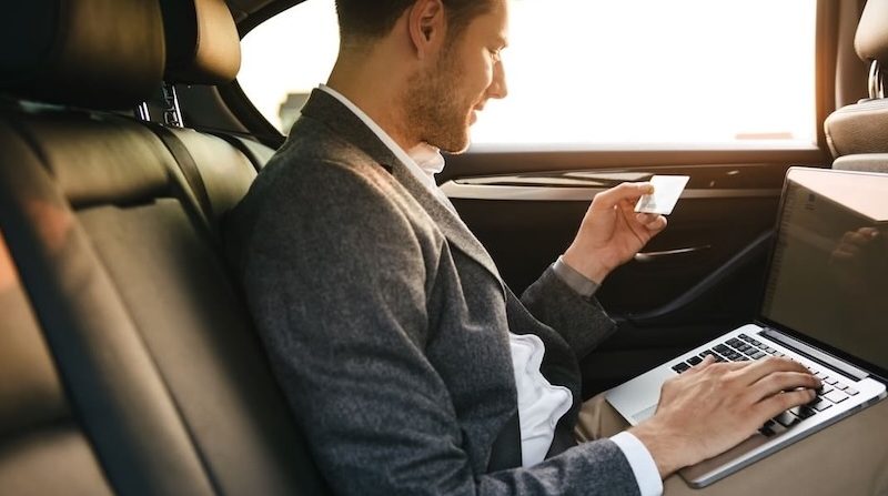 Geschäftsmann im Auto nutzt Laptop und hält eine Kreditkarte für eine Online-Transaktion