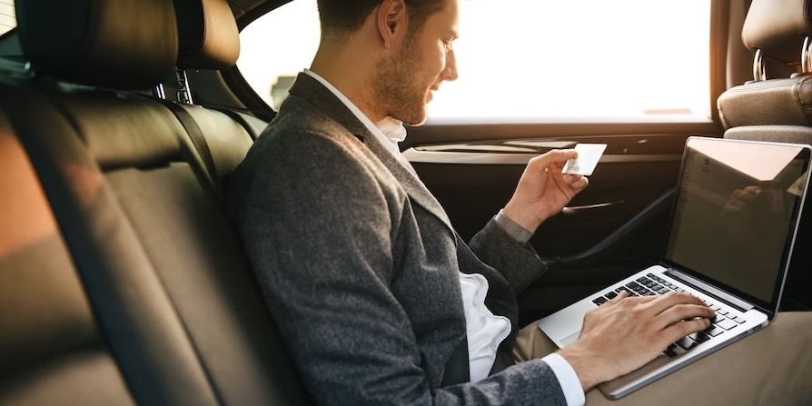 Geschäftsmann im Auto nutzt Laptop und hält eine Kreditkarte für eine Online-Transaktion