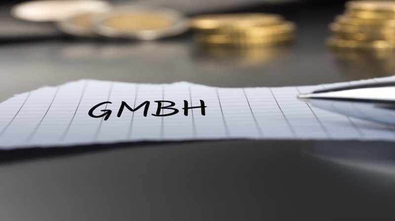 Zettel mit der Aufschrift GmbH neben einem Stift und Münzstapeln auf dem Tisch