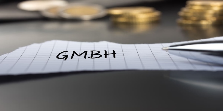 Zettel mit der Aufschrift GmbH neben einem Stift und Münzstapeln auf dem Tisch