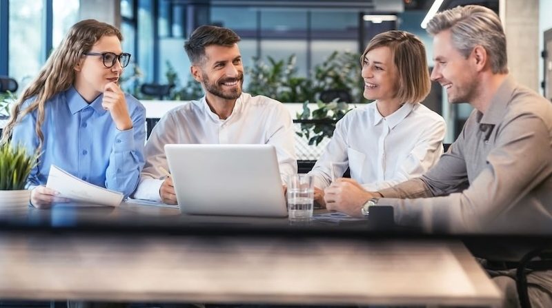 Gruppe von Geschäftspersonen sitzt im modernen Büro und bespricht ein Projekt am Laptop
