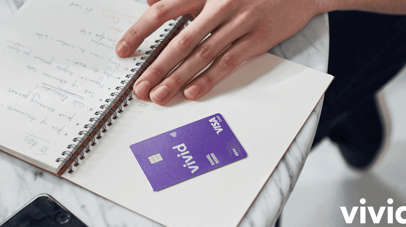 Hand liegt auf Notizbuch, daneben eine violette Vivid Visa Karte