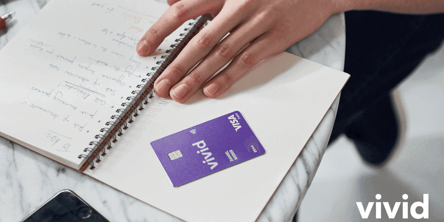 Hand liegt auf Notizbuch, daneben eine violette Vivid Visa Karte